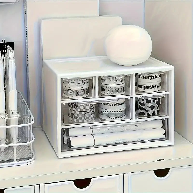 Organisateur de bureau en plastique blanc avec tiroirs transparents, comprenant plusieurs compartiments pour ranger des rouleaux de ruban washi décoratif et des stylos enroulés.