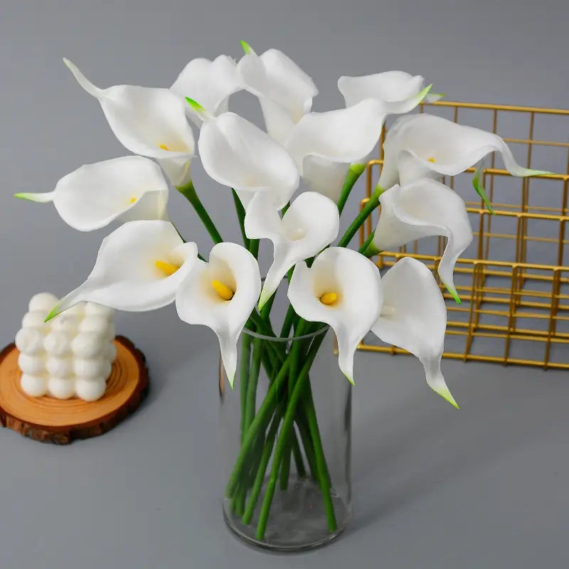 A front view of an artificial calla lily flower bouquet with white petals and yellow centers arranged in a clear glass vase for home decor.
