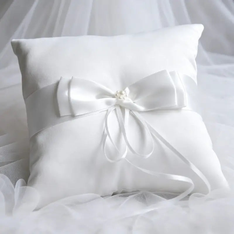 White satin ring pillow with decorative bow and pearl embellishment in a wedding flower basket and ring pillow set.