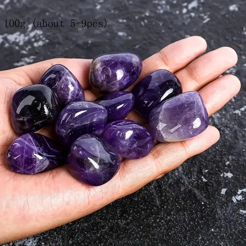 Une main tient un lot de pierres roulées naturelles polies et lisses d’améthyste, pesant 100 grammes, dans des nuances variées de pourpre profond et de violet, destinées à des soins de reiki.