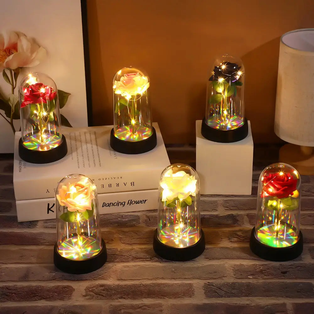 Cinq dômes en verre lumineux, chacun contenant une rose préservée avec des guirlandes lumineuses intégrées, projetant des reflets colorés sur la base dans le cadeau de fleur lumineux en dôme de rose éternelle.