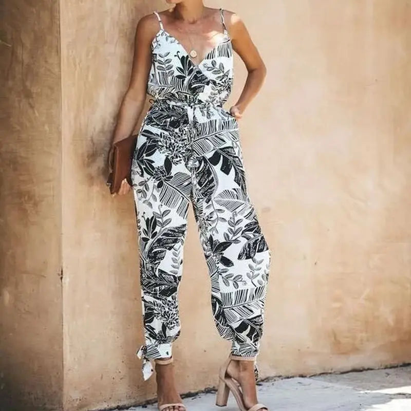 Ein Boho-Sommeroverall mit Blumendruck aus schwarzen und weißen tropischen Blättern: schmale Spaghettiträger, V-Ausschnitt und gesäumte Knöchel.