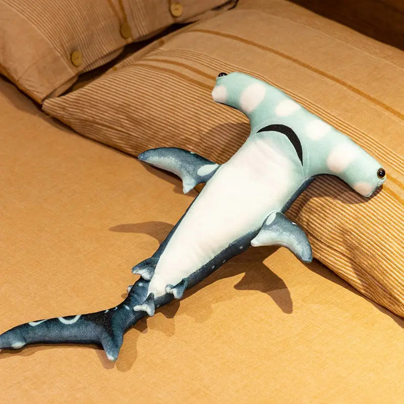 A soft light blue and white plush hammerhead shark pillow soft toy with black accents on its gills and fins.