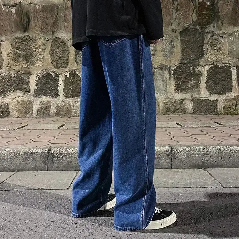 Jeans en denim bleu foncé à jambes larges pour hommes, avec un style streetwear coréen ample, une coupe droite et un ourlet légèrement effiloché.