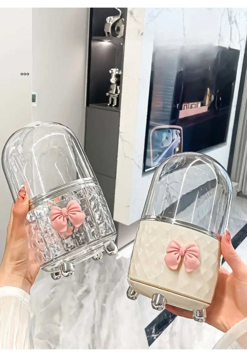 Organisateur tournant pour maquillage en verre transparent en forme de dôme, avec un nœud rose et des pieds argentés, pour le rangement des accessoires de maquillage.