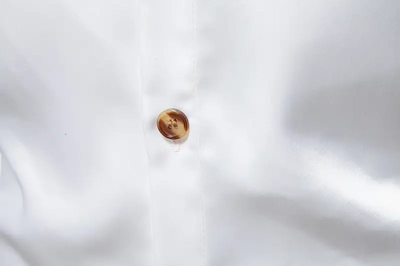 Ein runder, durchscheinender bernsteinfarbener Knopf mit leichtem Schimmer und vier kleinen Einbuchtungen an einem Herrenhemd mit goldfarbenem Besatz aus Satin.