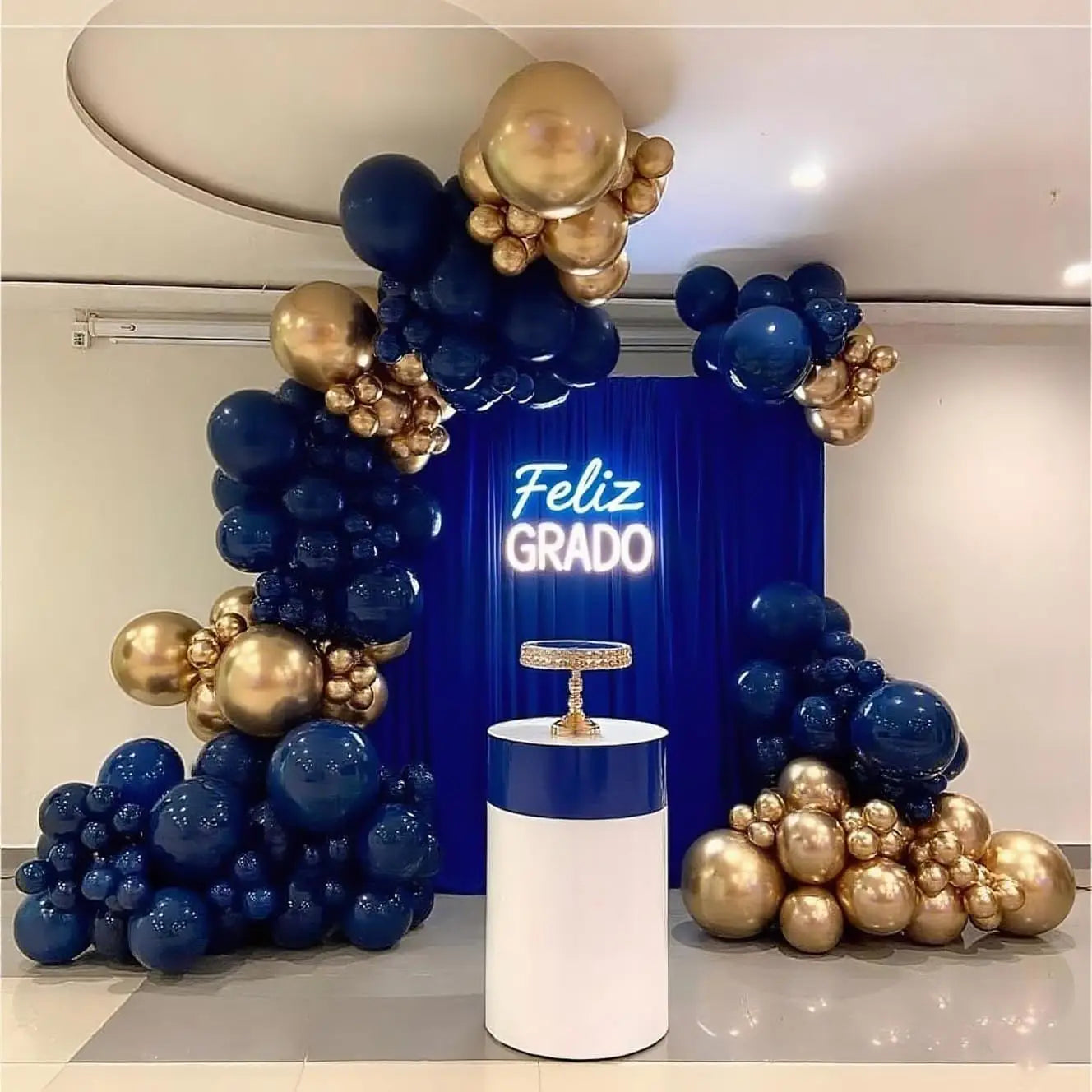 Navy blue and gold balloon arch kit featuring a central white pedestal with an ornate cake stand for elegant event decoration.