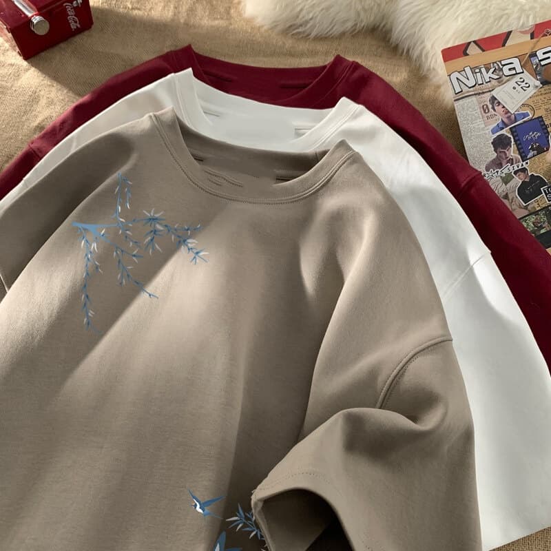 Camiseta de algodón oversize beige con delicados motivos de bambú bordado en azul y pájaros en la parte delantera.