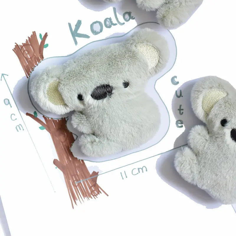 刺繍された黒い目と鼻が付いた、布製のやわらかな薄いグレーのコアラのピン型おもちゃです。インタラクティブなかわいい動物の笛（スウィーカー）おもちゃタイプとしてデザインされています。
