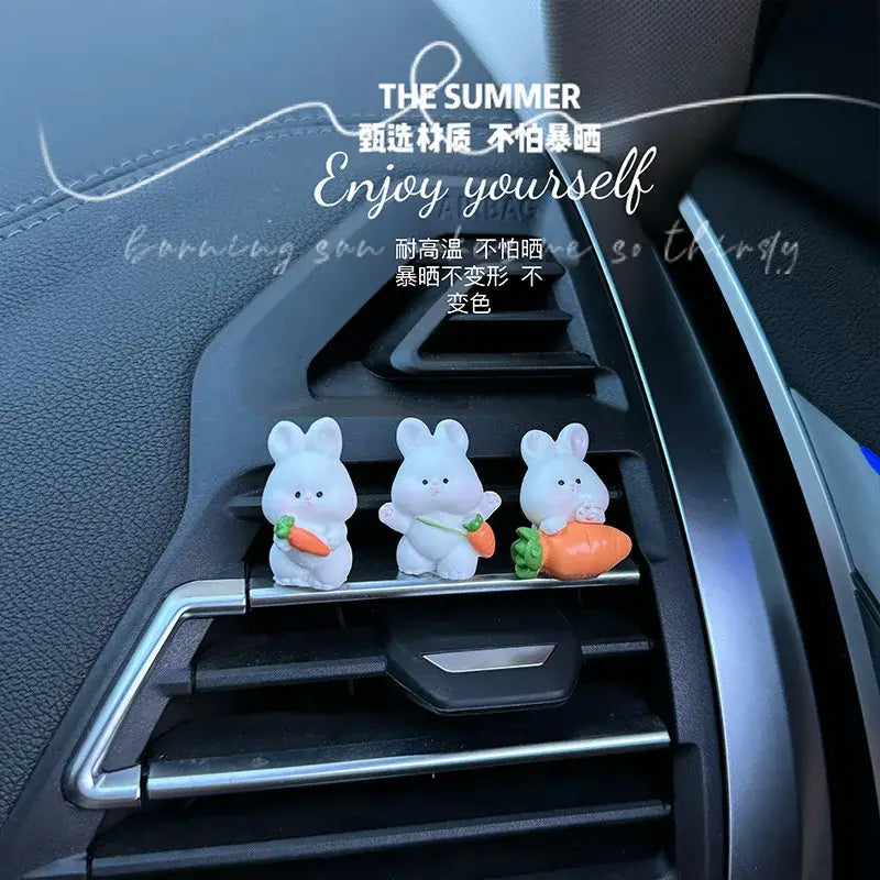 Trois figurines de lapin en plastique blanc, chacune tenant une carotte disposée sur une grille d’aération de voiture, comme des ornements de tableau de bord de voiture en forme de lapin mignon