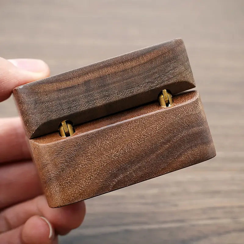 Boîte à bague en bois brun foncé avec finition polie lisse et deux fermoirs métalliques ton or pour conserver la proposition d’engagement.