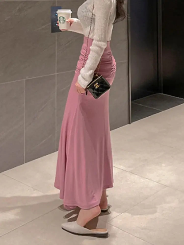 Schwarze Chanel Mini-Umhängetasche mit goldener Hardware und Kettenriemen, kombiniert mit einem rosafarbenen gerafften Meerjungfrauen-Midirock mit hoher Taille.