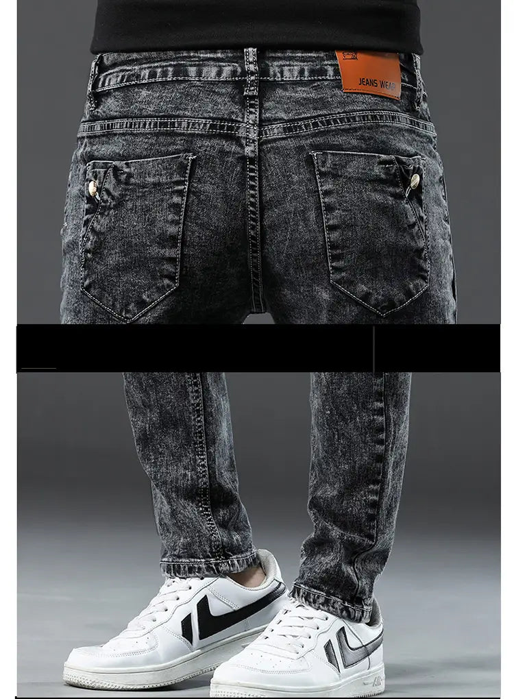 Jeans slim en denim extensible vintage pour hommes, lavage gris, en denim gris foncé usé, avec lavage délavé et surpiqûres visibles, assorti à des baskets blanches.
