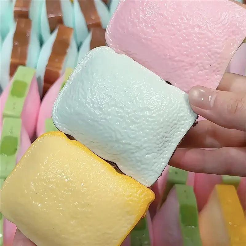 Pastellfarbene rechteckige Buttersticks als ASMR-Sensory-Squishy-Spielzeuge mit einer strukturierten Oberfläche, die an Marshmallows erinnert; entworfen zur Stresslinderung und zum sensorischen Spiel.