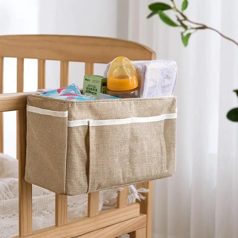 beiges gewebtes Stoff-Bettgestell-Organisationssystem für das Babybett mit weißem Abschluss und mehreren Taschen, ausgelegt als Aufbewahrungstasche für neben dem Bett (Mehrtaschen-Organizer) zur Organisation im Kinderzimmer.