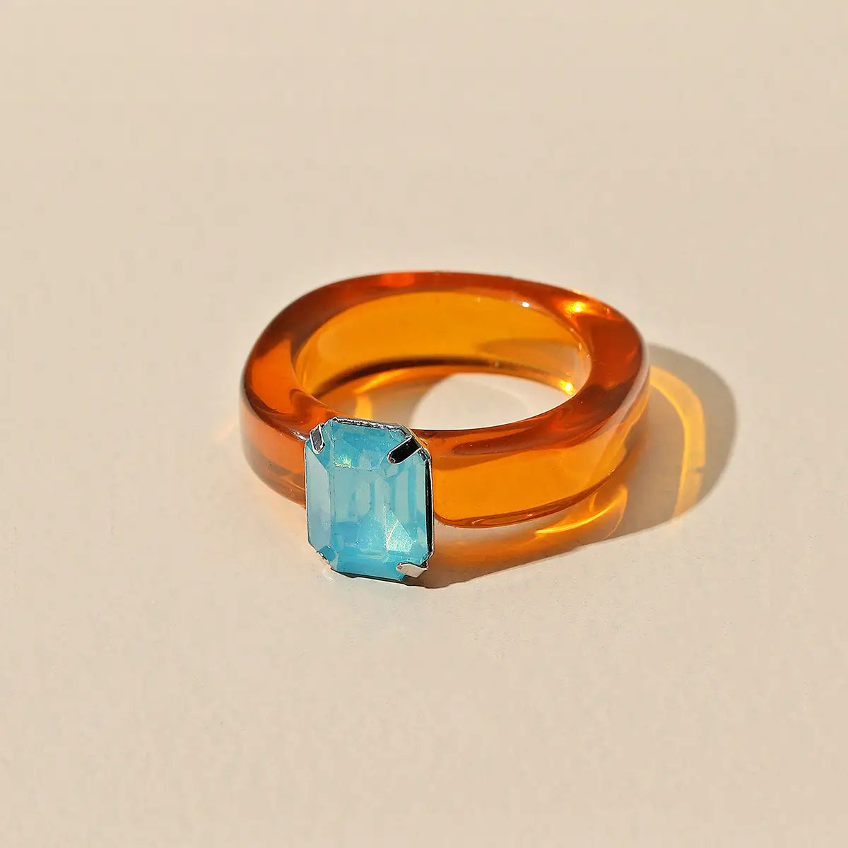 Colorful resin crystal geometric ring for women featuring a vibrant orange translucent band with a striking blue emerald-cut stone set in silver-toned metal.