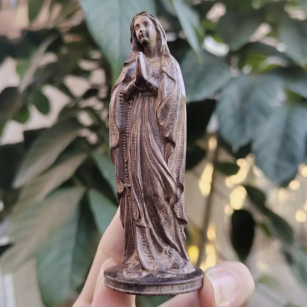 Statuette de la Vierge Marie en bois finement sculpté à la main, avec des vêtements détaillés et une expression sereine dans un bois brun naturel.