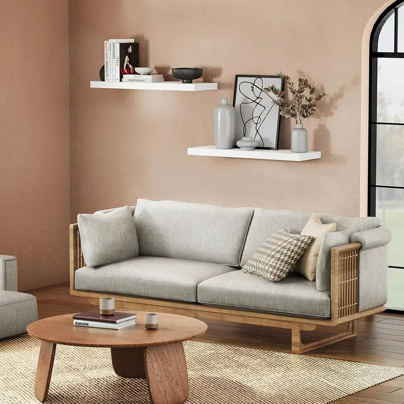 Light gray upholstered sofa with wooden frame and slatted side panels positioned near floating shelves for living room wood wall display.