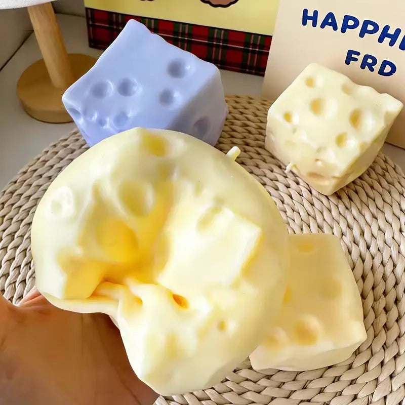 un juguete blando de descompresión de crecimiento lento con forma de queso de color amarillo pálido, con orificios característicos y una textura blanda y que se hunde, visto desde el frente.