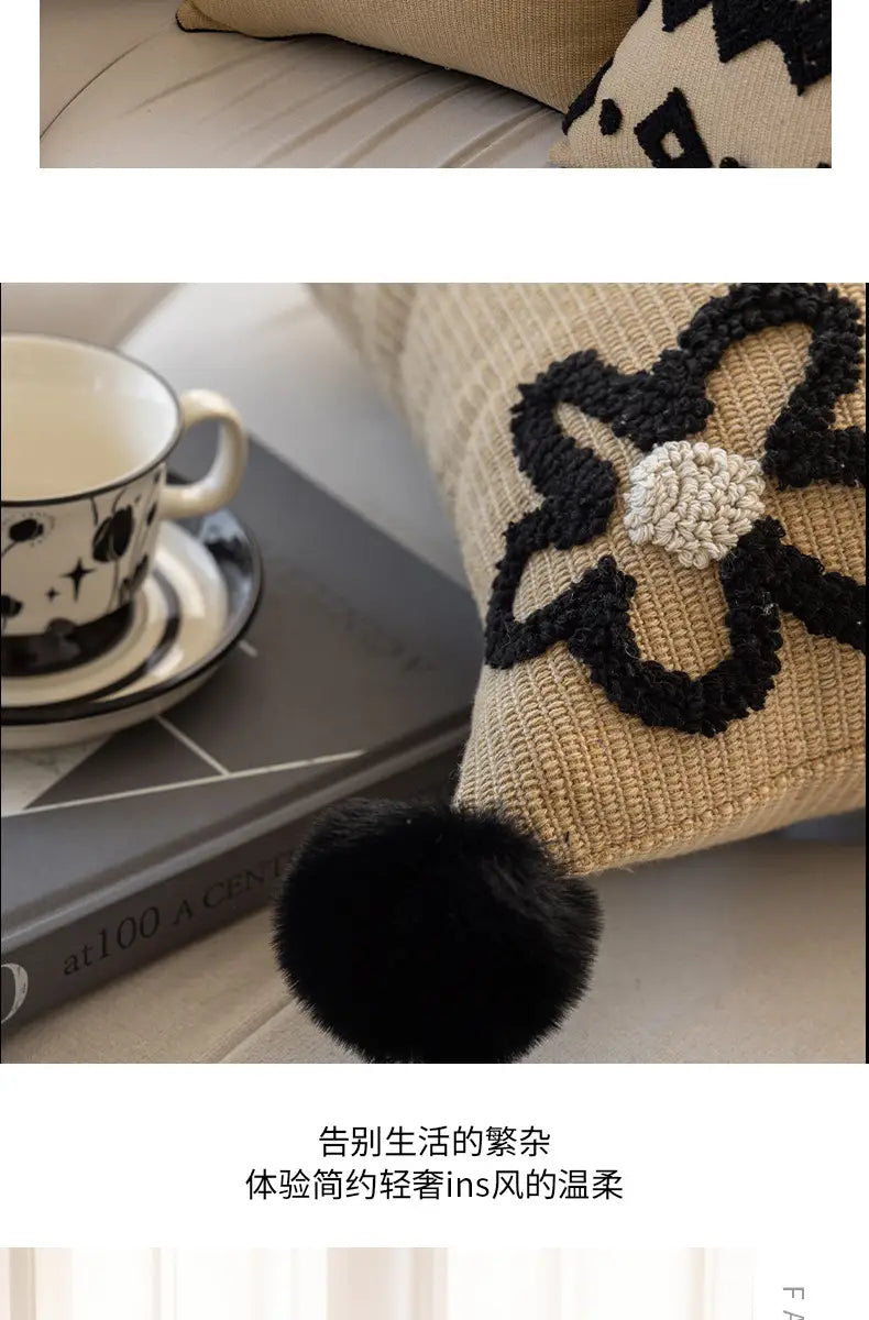 Housse de coussin bohème beige texturée, avec un motif floral brodé en noir, un centre crocheté blanc et un pompon noir moelleux, pour la décoration du salon.