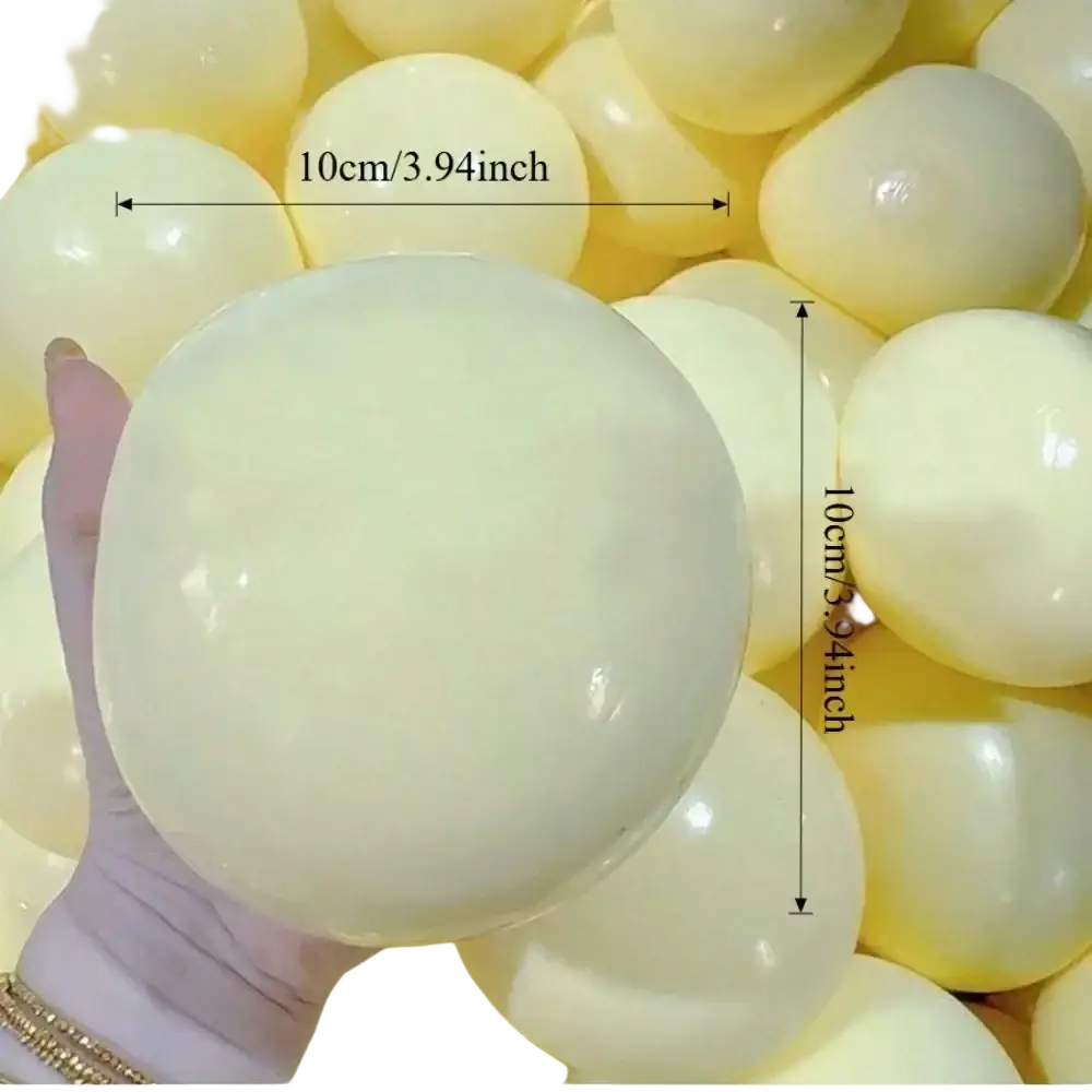 A hand holds a pale yellow glossy stress relief squishy ball viewed from the front with a smooth surface