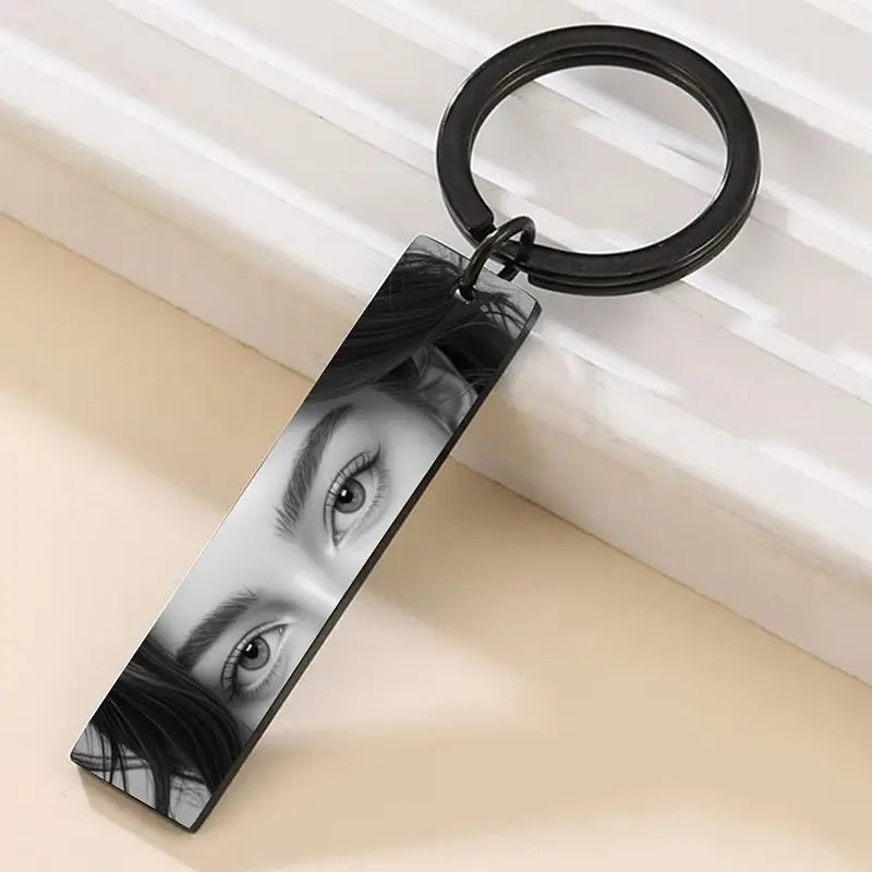 Black rectangular stainless steel keychain featuring a custom eye photo engraved in black and white with dark hair detail, attached to a matching black ring.