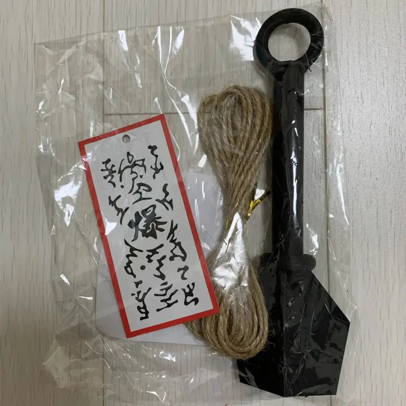 schaufel aus schwarzem Kunststoff mit geschlungener Griffschlaufe und natürlichem Bindfadenbündel, neben einem Ninja-Kunai-Kühlschrankmagneten aus PVC, Shuriken-Spielzeug, ausgestellt.