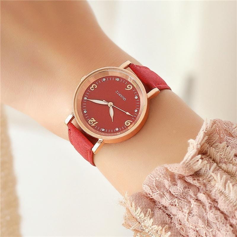 A rose gold-toned women quartz watch with a vibrant red dial, matching red suede leather band, and diamond-like hour markers.