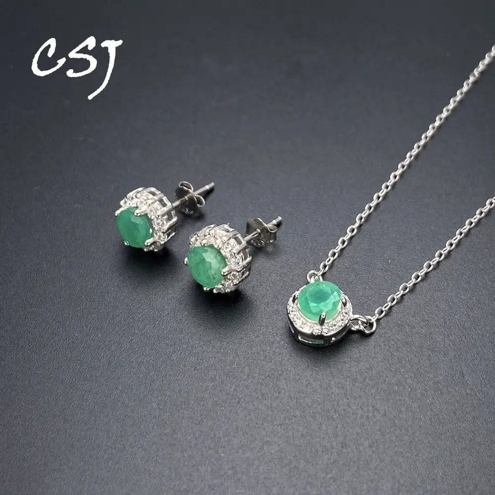 Elegant emerald sterling silver jewelry set featuring a pendant necklace and matching stud earrings with vibrant green stones surrounded by sparkling diamonds.