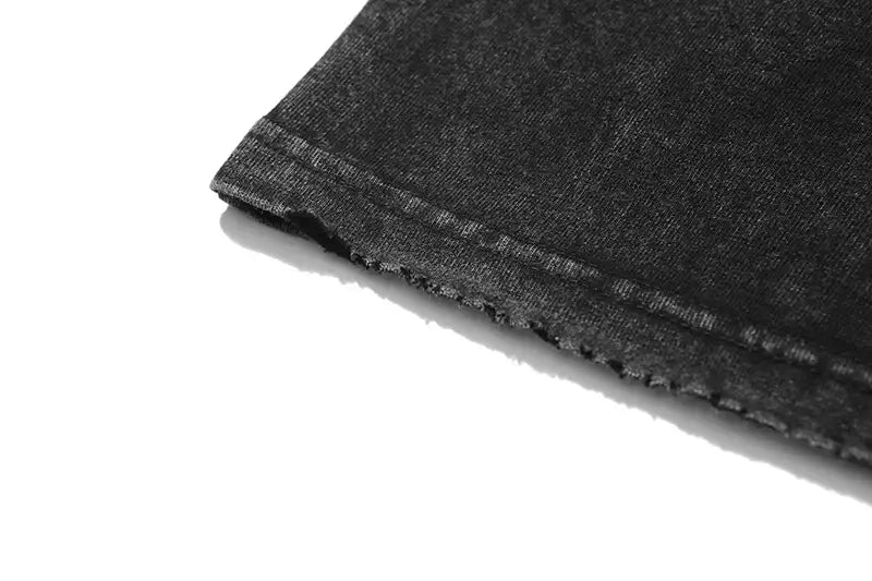 Tela de mezclilla (denim) negra con textura ligeramente desgastada y costuras visibles en el dobladillo, en una camiseta extragrande vintage lavada y desteñida con gráfico de anime gótico.