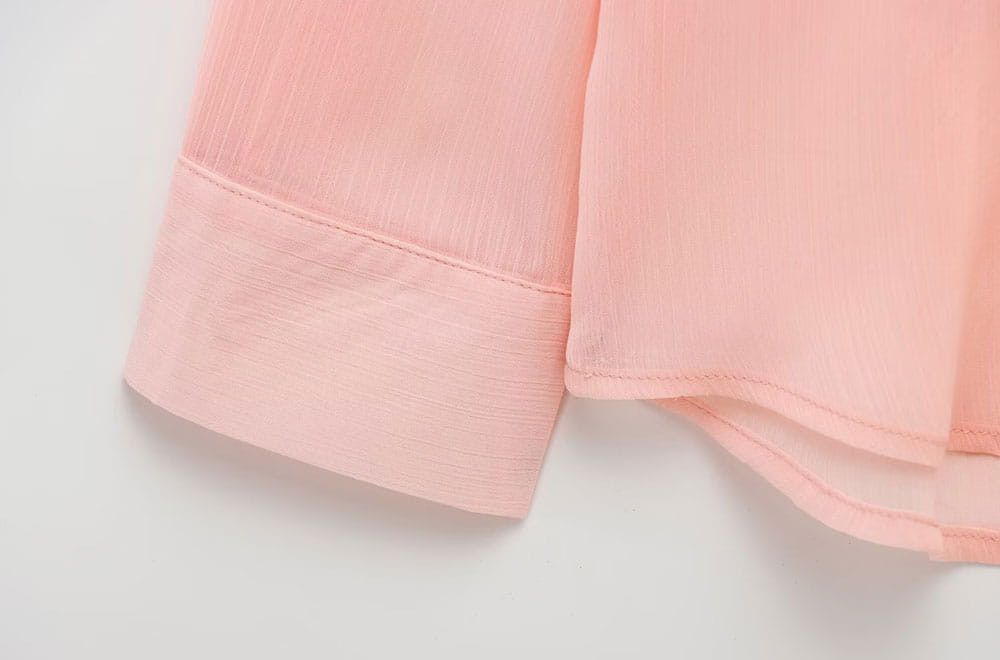 Soft pink textured ruffled button up blouse featuring a chiffon sleeve with a neatly rolled cuff.