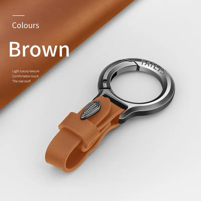 Brown leather car keychain with metallic silver-toned circular clip and small engraved leaf charm emblem.