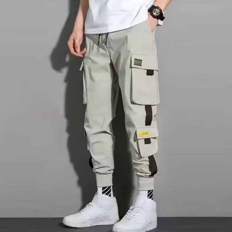 Pantalons cargo beige pour hommes avec plusieurs poches et accents noirs et jaunes sur les côtés, conçus comme des sweatpants décontractés à cordon de serrage.