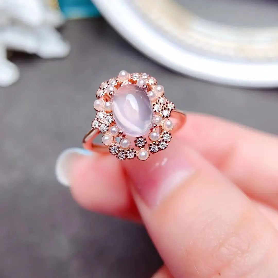 Une bague délicate en or rose de l’ensemble de bijoux en argent sterling avec quartz rose, présentant au centre une pierre de lune rose ovale entourée d’un halo de petits diamants et de perles d’eau douce.