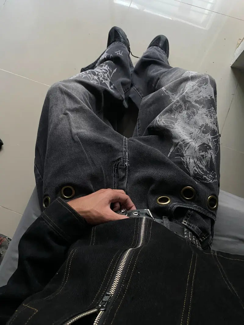 Black denim Y2k gothic graphic wide leg jeans for men featuring distressed white prints and gold-toned metal eyelets.