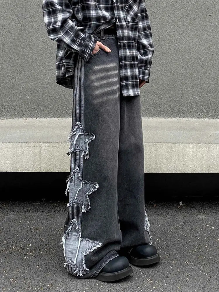 Pantalon en denim wide-leg gris foncé avec un motif de patchwork en forme d’étoile délavé et déchiré le long de la couture extérieure, dans un style y2k baggy distressed denim jeans.