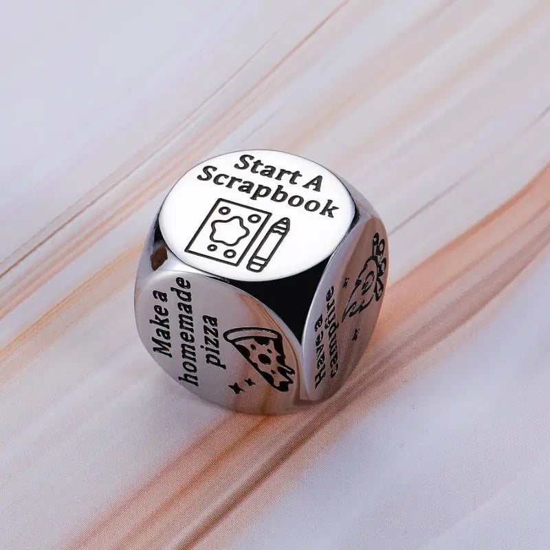 Silver metallic six-sided stainless steel food decision dice for couples date night engraved with activities like start a scrapbook and make a homemade pizza.