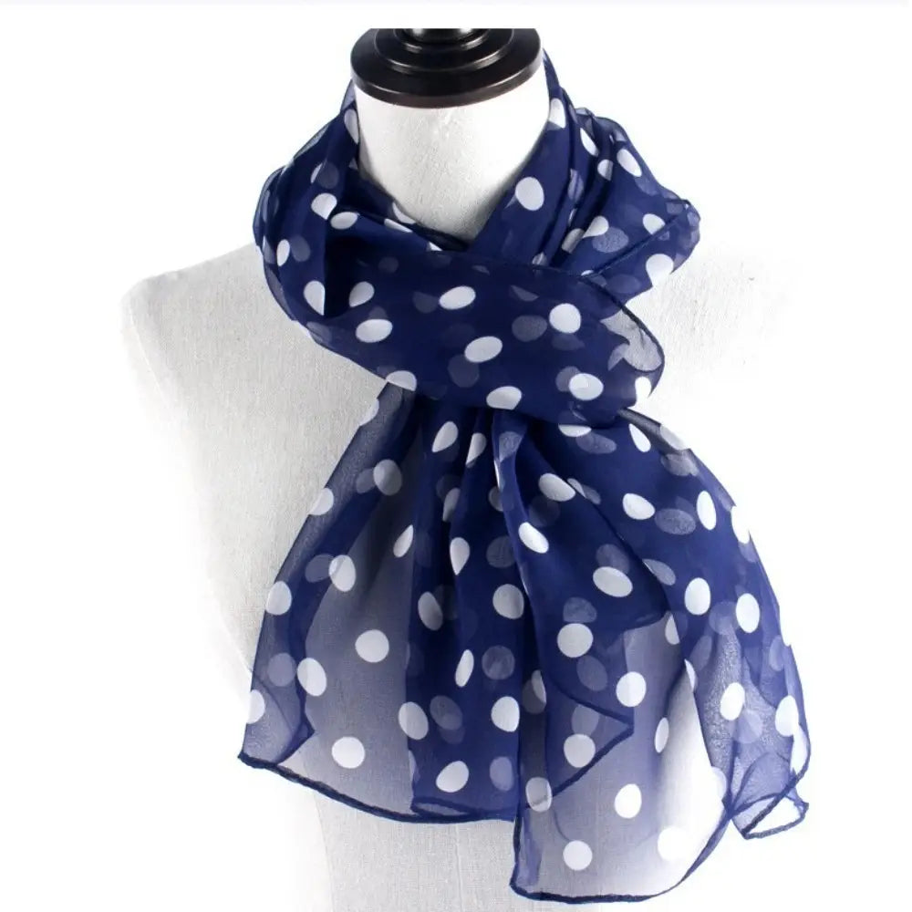 A navy blue sheer silk head wrap scarf with white polka dots draped elegantly around a mannequin neck.