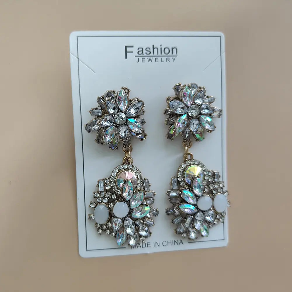ホワイトのオパールのようなストーンをアクセントに、きらめくクリアと虹彩感のあるクリスタルで装飾されたクリスタル・ラインストーンのステートメントネックレスセット。そこから生まれたシャンデリア風のエレガントなシルバートーンのイヤリング。