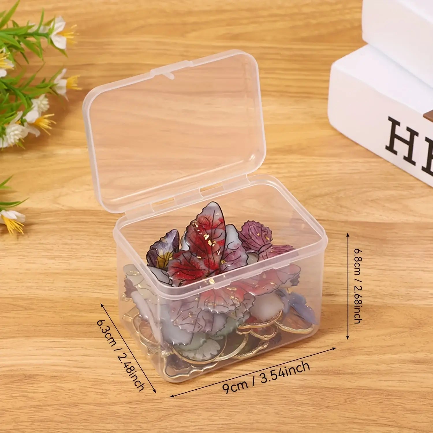 Boîte de rangement en plastique transparent contenant plusieurs broches colorées en forme de fleurs en verre ou en résine, conçues pour organiser des travaux manuels et des strass.