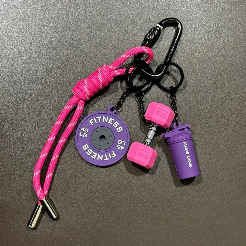 A vibrant pink and purple fitness keychain featuring a circular weight plate, miniature dumbbells, and a shaker bottle charm as a colorful gym bag accessory.