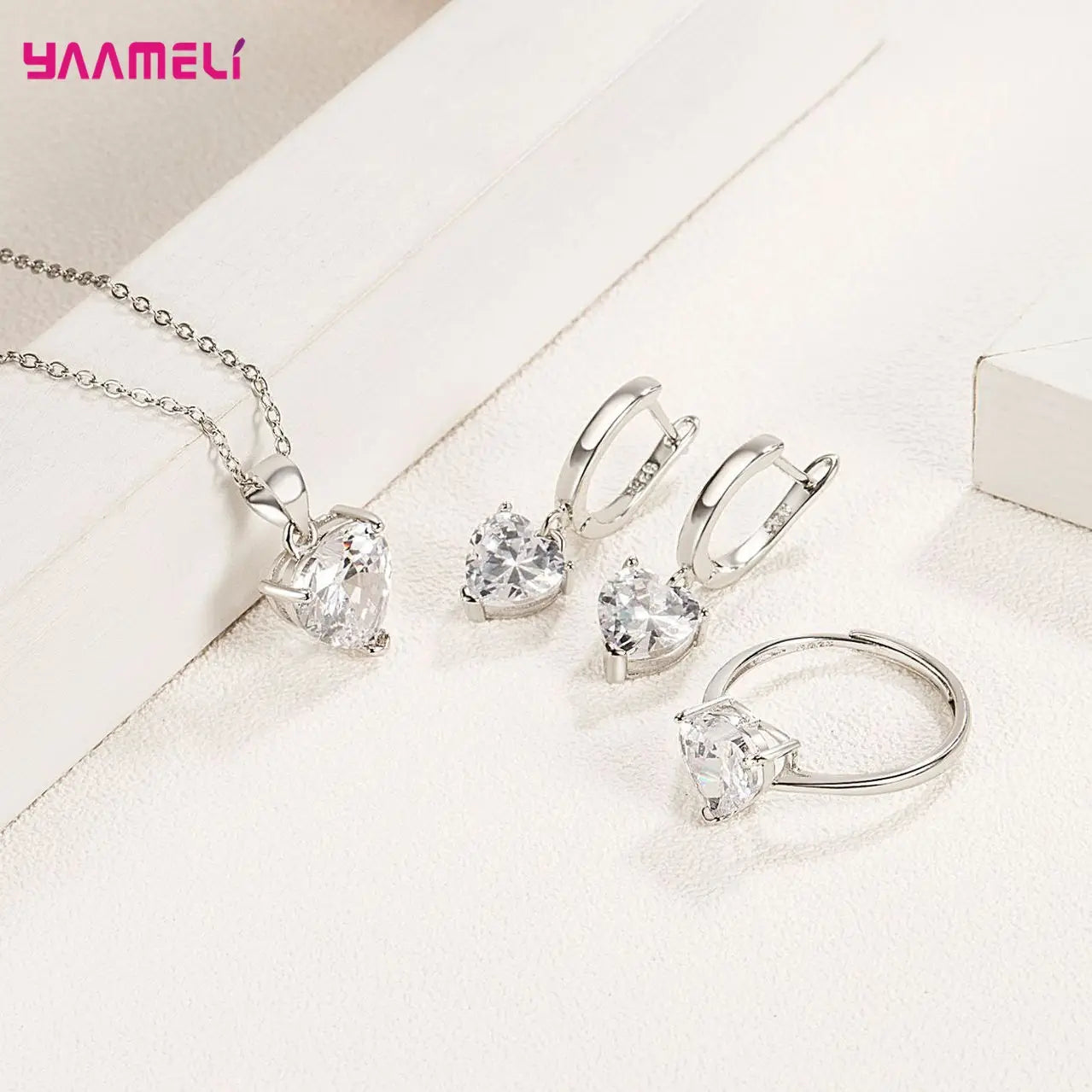 Sterling silver heart jewelry set featuring a silver heart-shaped crystal pendant necklace with matching zircon huggie earrings and ring set.