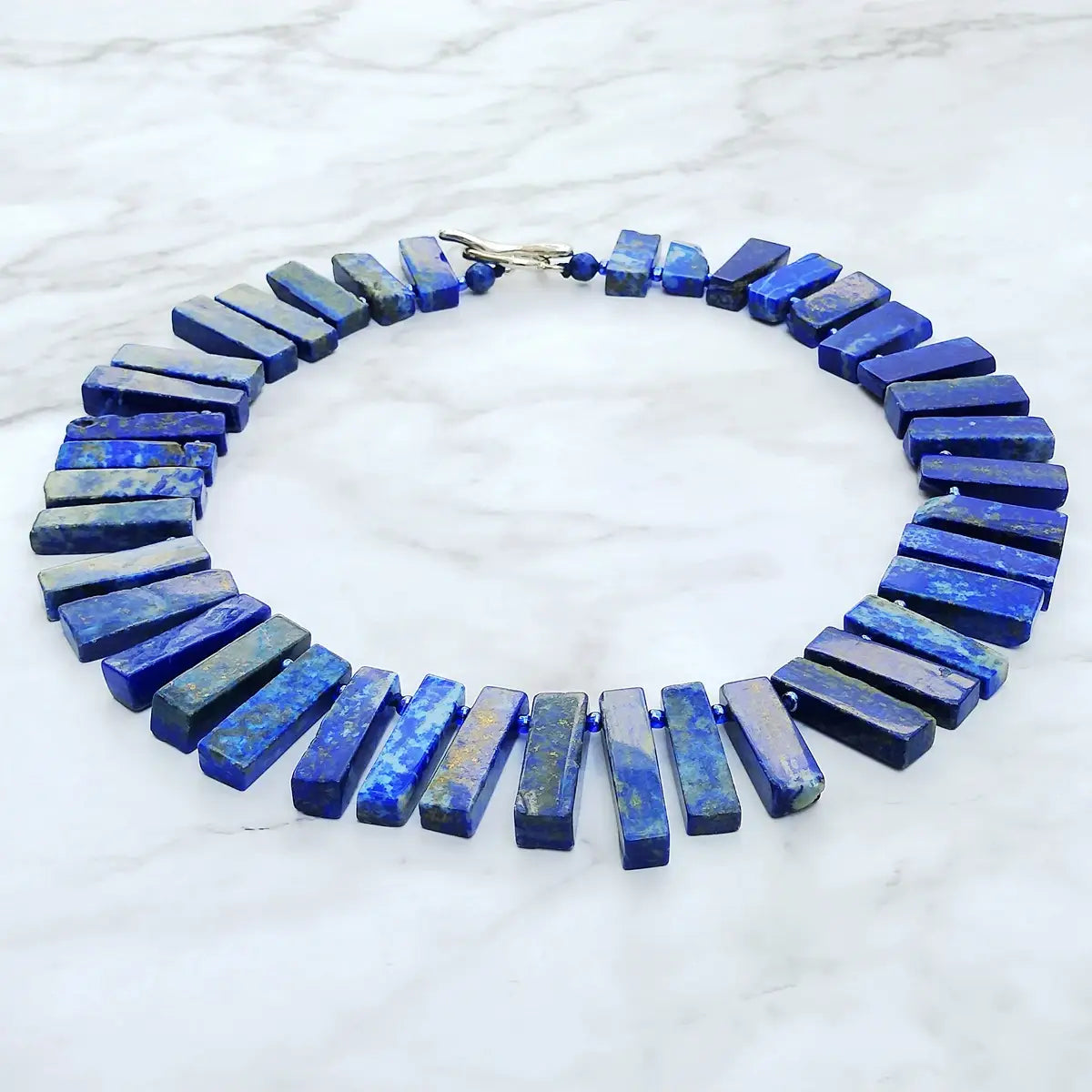 Un collier ras du cou audacieux en lapis-lazuli bleu profond, composé de perles de pierres précieuses rectangulaires à veines naturelles et d’une fermeture à tons argentés pour une bijouterie de déclaration.