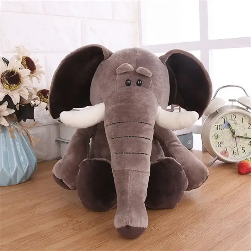 Un elefante gris de peluche relleno con orejas grandes caídas, colmillos blancos y detalles faciales cosidos de la colección de juguetes blandos de león, elefante y tigre.