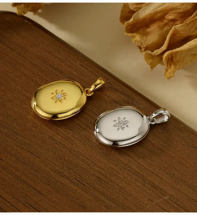 中央にダイヤモンドをあしらい、刻印の花柄およびゴールド スター バースト ロケット ネックレス コレクション内のエッチングされた花の模様を備えた、2つの楕円形のゴールド／シルバーロケットペンダントです。