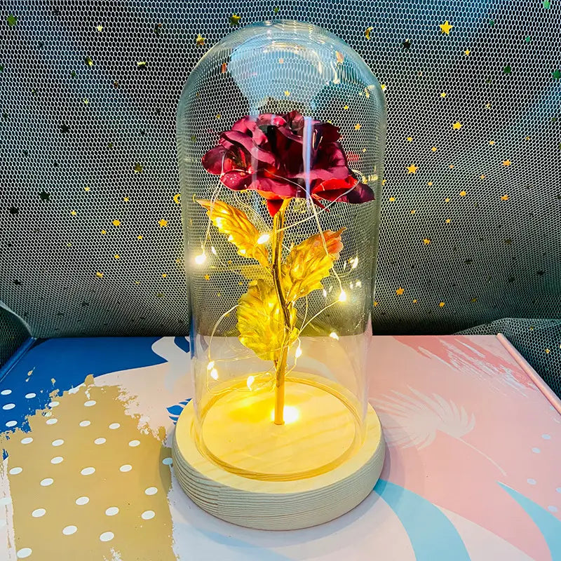 Eine leuchtend rote Rose mit goldenen Blättern und Stiel, umschlossen in einer klaren Glaskuppel auf einem Holzsockel, im „Eternal Gold Rose Glass Dome Led Light Gift“