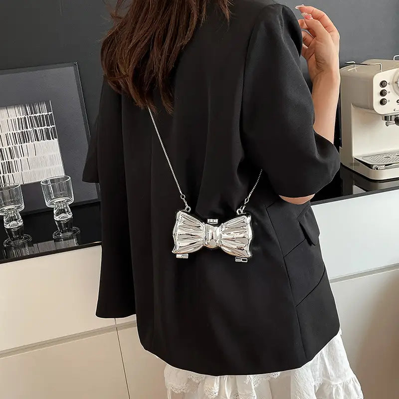 pochette en métal argenté en forme de nœud avec anse à chaîne, conçue comme accessoire de bandoulière dans le style de pochette à nœud en métal doré