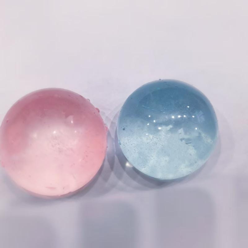 Zwei transluzente kugelförmige Fidget-Spielzeug-Stressabbau-Bälle in zartem Rosa und mit Verlauf in Blau mit weißen Sprenkeln, hergestellt aus TPR-Material, das mit Kokosöl angereichert ist.