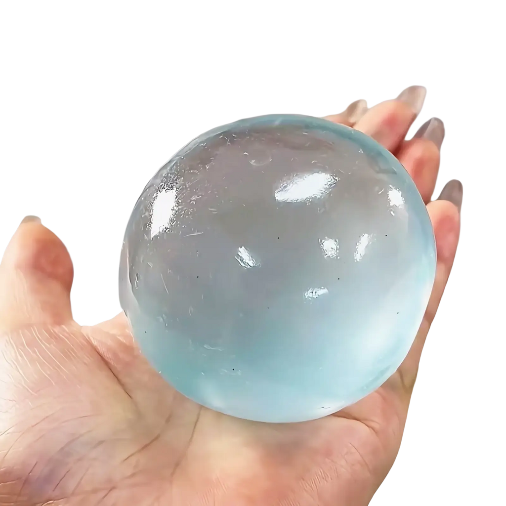 A translucent light blue blue coconut oil stress ball squeeze toy with a smooth glossy surface and subtle internal reflections held in hand