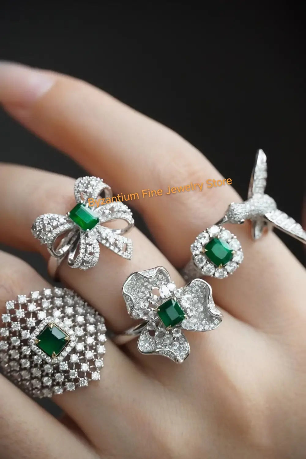Eine Hand präsentiert eine elegante Kollektion von Smaragd- und Diamantbesetzten Ringen mit einem schalenförmigen Ring, der von Pavé-Diamanten umgeben ist, neben dem grünen Edelstein, kombiniert mit Ohrringen mit silbernen Tropfenquasten in Gold-Vermeil.